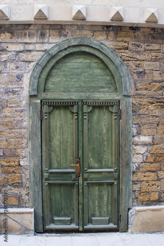 Old beautiful green wooden door in a stone wall in the form of an arch.