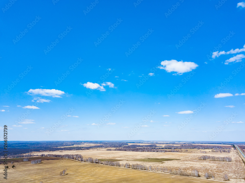 Panorama from the air on the lush meadows and fields with colorful plots of agricultural crops before sowing in spring outside the city in the sun under a blue sky and white clouds. Nature in season.