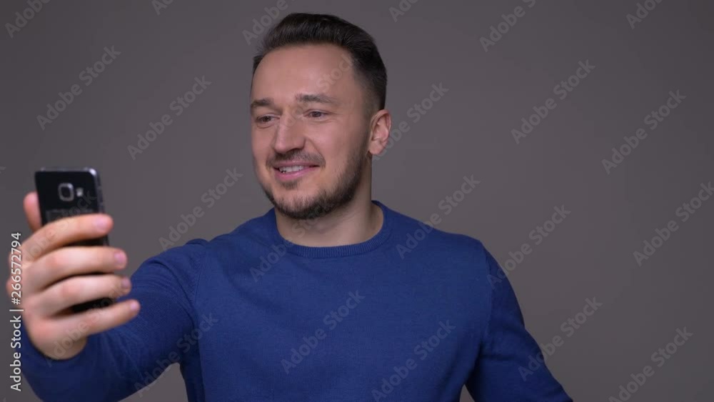 Closeup shoot of young handsome caucasian man having a video call on the phone in front of the camera with background isolated on gray Closeup shoot of young handsome caucasian man having a video call on the phone in front of the camera with background isolated on gray