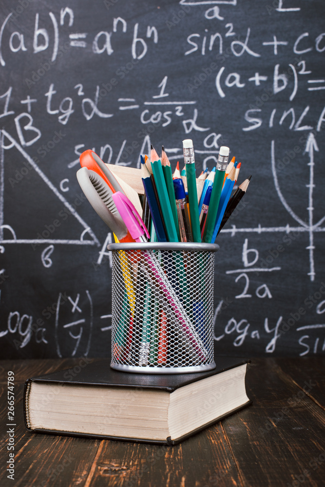 Books and stand for pens on a wooden table, against the background of a chalk board with formulas. Teacher's day concept and back to school. Books and stand for pens on a wooden table, against the background of a chalk board with formulas. Teacher's day concept and back to school.