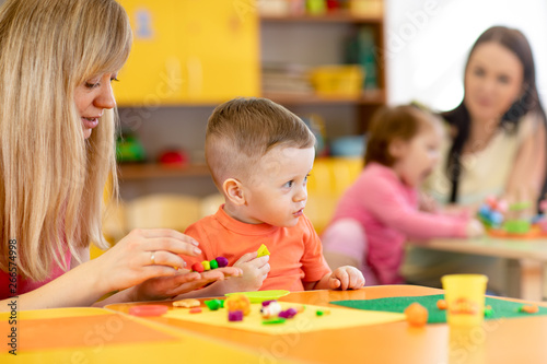 Kindergarten kid with teacher mould from plasticine on table in nursery