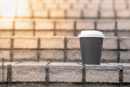 Close up of take away paper cup of hot coffee on stone tile stair.