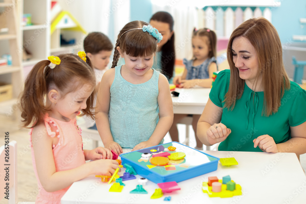 Children kids and teacher playing with constructor on table in kindergarten Children kids and teacher playing with constructor on table in kindergarten