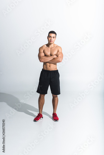 handsome sportive mixed race man in black shorts and red sneakers looking at camera on white