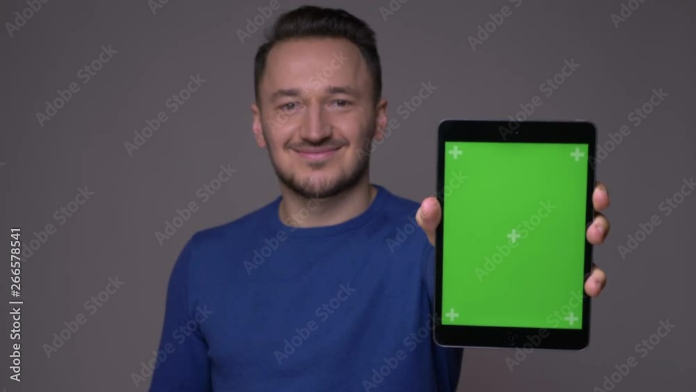 Closeup shoot of young handsome caucasian man using the tablet and showing green chroma key screen to camera with background isolated on gray Closeup shoot of young handsome caucasian man using the tablet and showing green chroma key screen to camera with background isolated on gray