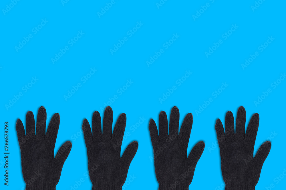 Horizontal row of four black warm woolen gloves on blue background with copy space for your text. Top view