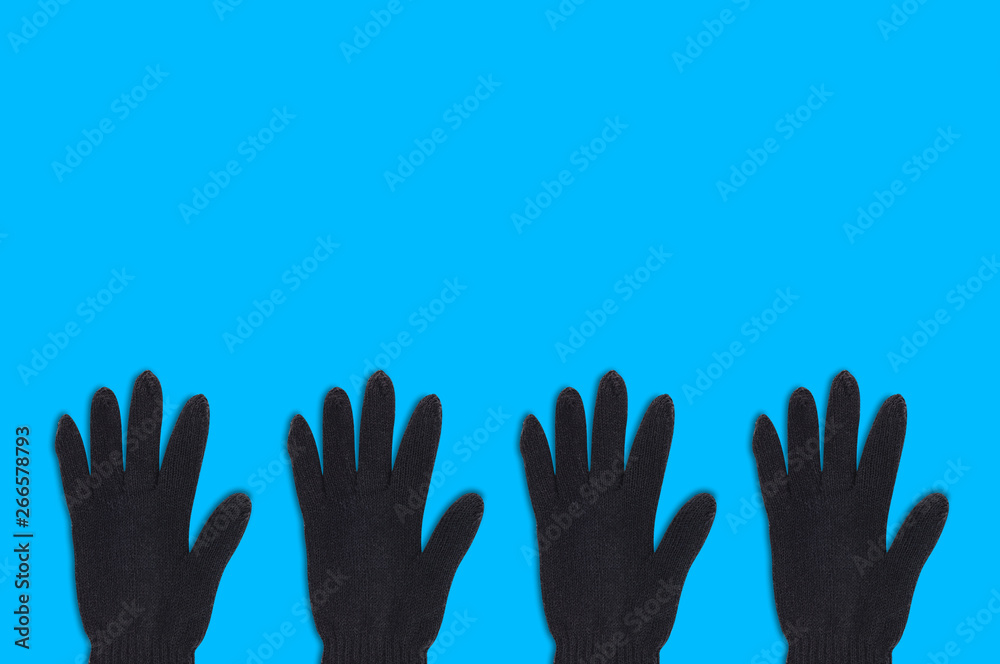 Fototapeta premium Horizontal row of four black warm woolen gloves on blue background with copy space for your text. Top view