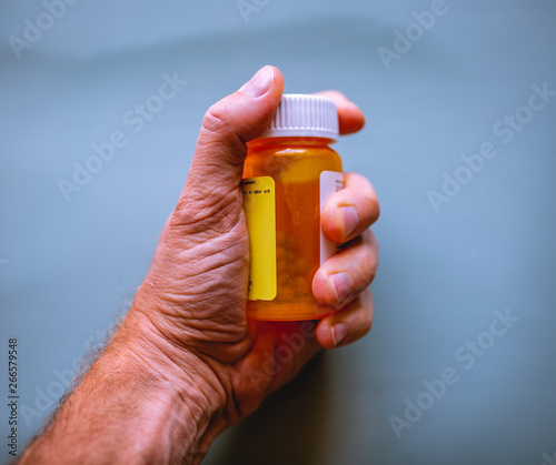 Man holds bottle of prescription pills in the palm of his hand. Health care or addiction concept.