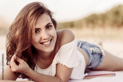 Summer portrait of a beautiful smiling girl on vacation, lying on the sand in the sun.