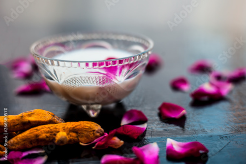 Milk face pack on black shiny surface consisting of raw milk,turmeric or haldi and badam in a glass bowl along with entire raw ingredients. photo