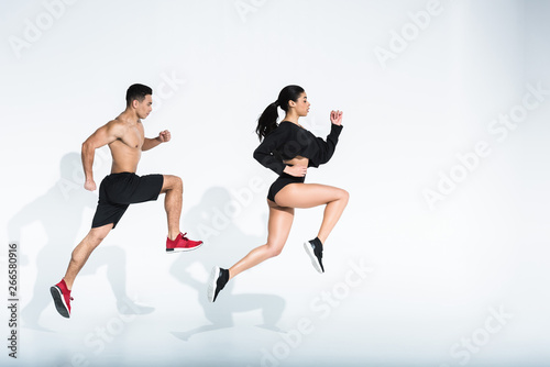 side view of sportive african american girl and athletic mixed race man running on white background