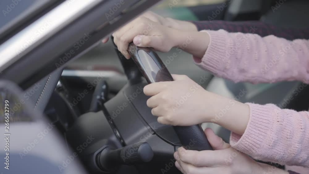 Close-up of the hands of the father and daughter sitting behind the wheel of a luxury car. Father teaches girl to drive a vehicle. Close-up of the hands of the father and daughter sitting behind the wheel of a luxury car. Father teaches girl to drive a vehicle.