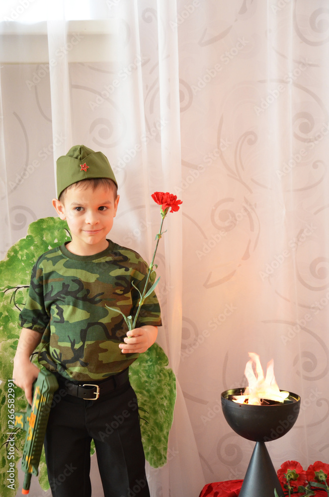 A boy in a military T-shirt and field cap with a carnation flower near the eternal flame. Victory Day celebration in Russia on May 9. Boy at the eternal flame of the soviet soldier at the Glory