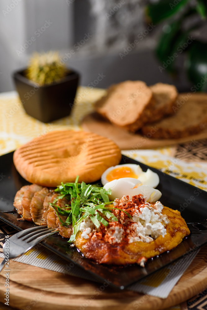 Delicious breakfast with boiled eggs, pumpkin puree, lettuce, cheese and fresh bread on a black plate on a yellow set on a wooden table in a restaurant. Close up. Space Delicious breakfast with boiled eggs, pumpkin puree, lettuce, cheese and fresh bread on a black plate on a yellow set on a wooden table in a restaurant. Close up. Space
