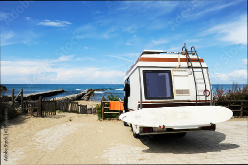 Rear of vintage camper parked on the beach (seaside) with a surfboard on back - Leisure trip in the summer.