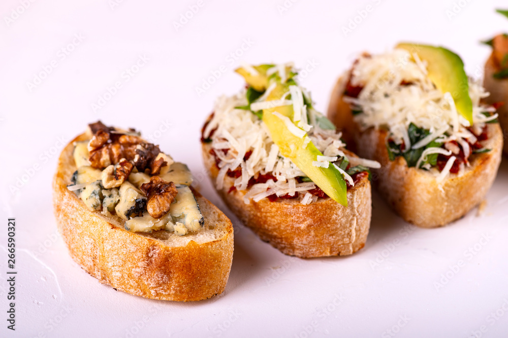 Brushetta set for an aperitif. Variety of small sandwiches with tomatoes, parmesan cheese, avocado and walnut served on a white background Brushetta set for an aperitif. Variety of small sandwiches with tomatoes, parmesan cheese, avocado and walnut served on a white background