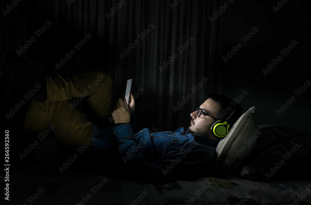 Man watching tv series in a tablet sitting on a bed in the night at home Man watching tv series in a tablet sitting on a bed in the night at home