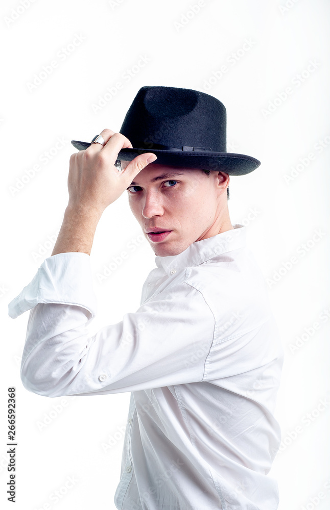 The guy in the white shirt and hat on a white background, the guy holds his hat with one hand, posing in the studio - isolated The guy in the white shirt and hat on a white background, the guy holds his hat with one hand, posing in the studio - isolated