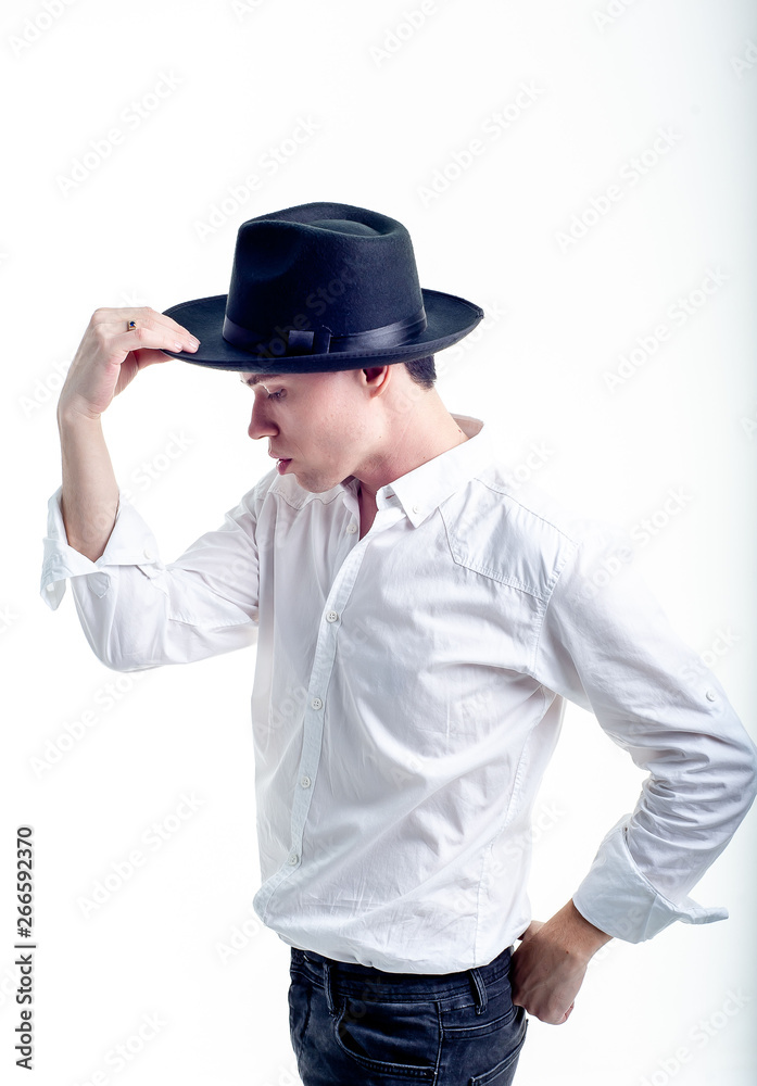 The guy in the white shirt and hat on a white background, the guy holds his hat with one hand, posing in the studio - isolated The guy in the white shirt and hat on a white background, the guy holds his hat with one hand, posing in the studio - isolated