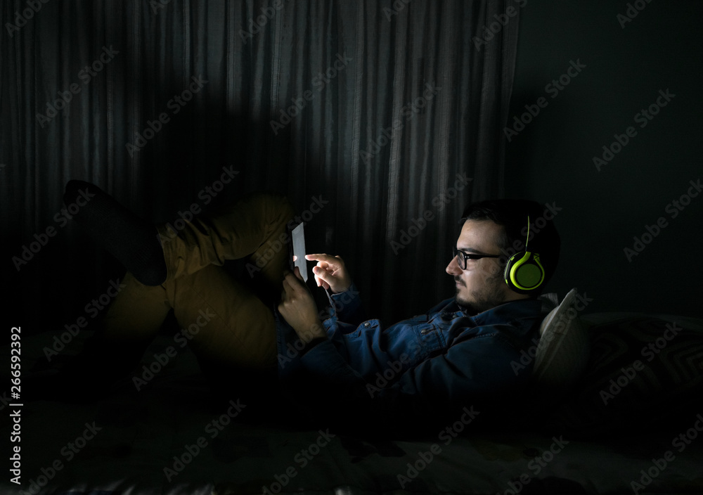 Man watching tv series in a tablet sitting on a bed in the night at home Man watching tv series in a tablet sitting on a bed in the night at home