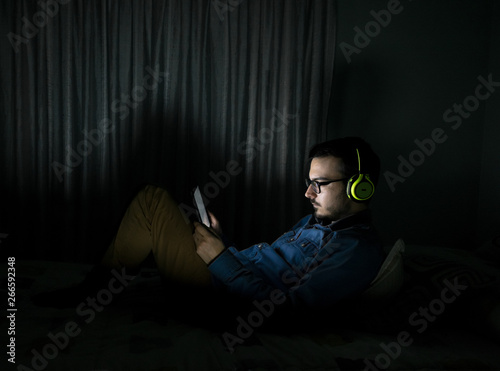 Man watching tv series in a tablet sitting on a bed in the night at home © Cristian Blázquez