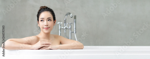 Panoramic banner image of young beautiful Asian lady relaxing and looking away while sitting in the bathtube.Spa treatments for beauty and health with skin care.wide crop. photo