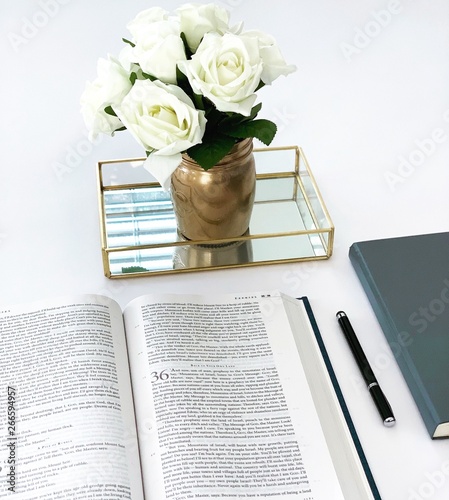 Baselland, Switzerland - 03.05.2019. Bible flat lay on a white Table with different accessories; white roses, grey journal, black pen, golden vase, etc. 