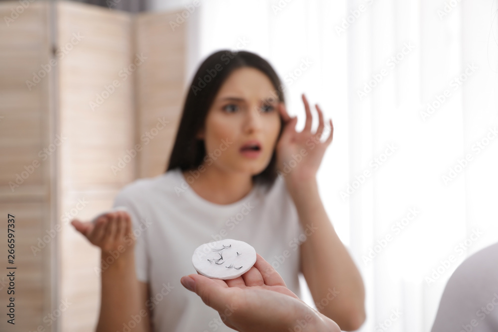 Beautiful woman holding cotton pad with fallen eyelashes near mirror indoors Beautiful woman holding cotton pad with fallen eyelashes near mirror indoors