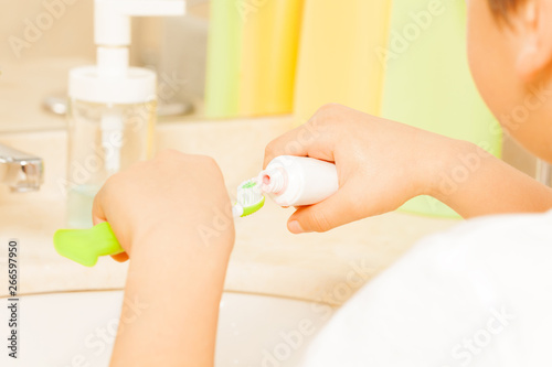 Kid spreading toothpaste on green toothbrush