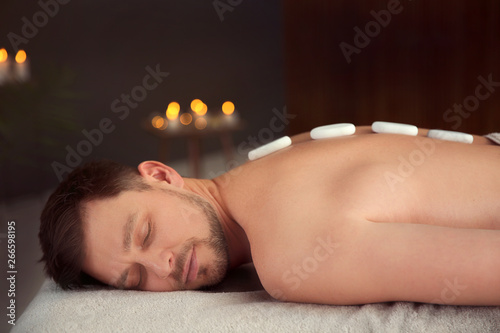 Handsome man receiving hot stone massage in spa salon