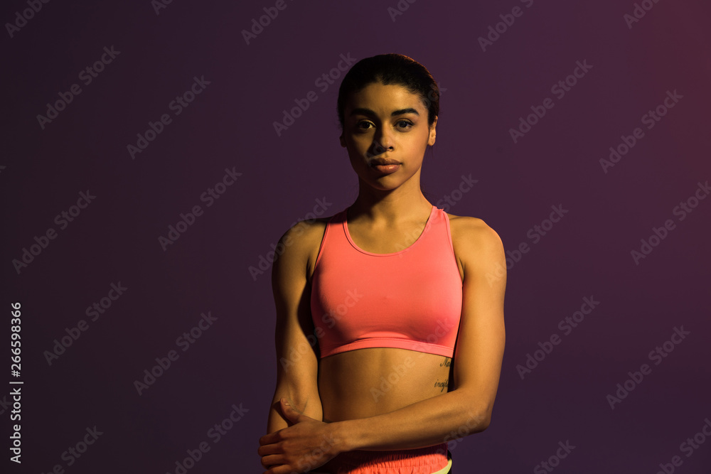 Obraz premium beautiful sportive african american girl in pink sports bra looking at camera isolated on purple