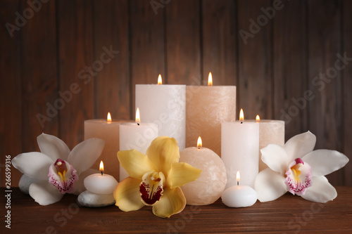 Beautiful composition with candles and flowers on table against wooden background