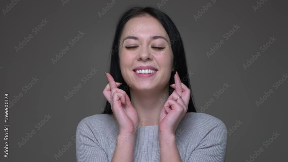 Closeup shoot of young pretty brunette caucasian female having her fingers crossed and being worried with background isolated on gray Closeup shoot of young pretty brunette caucasian female having her fingers crossed and being worried with background isolated on gray
