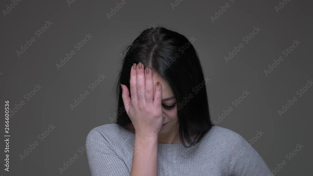 Closeup shoot of young angry brunette caucasian female clapping her head with a hand with embarrassment with background isolated on gray Closeup shoot of young angry brunette caucasian female clapping her head with a hand with embarrassment with background isolated on gray