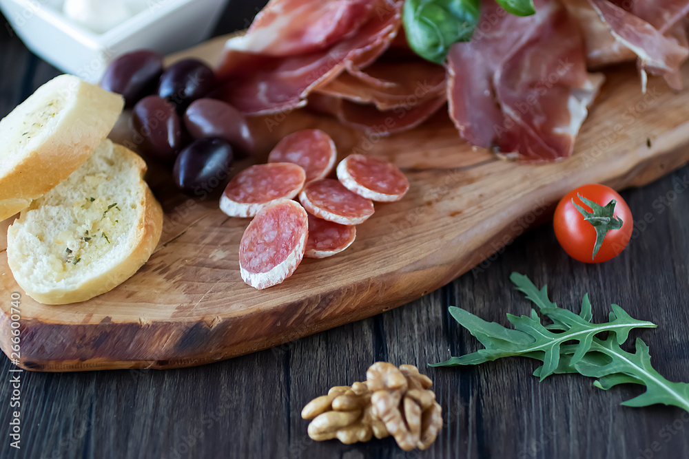 Prosciutto, bread, olives, walnut, salami, basil and cherry tomatoes on brown wooden board. Mediterranean kitchen. Prosciutto, bread, olives, walnut, salami, basil and cherry tomatoes on brown wooden board. Mediterranean kitchen.