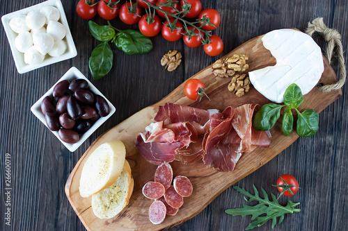 Prosciutto, bread, olives, walnut, salami, basil and cherry tomatoes on  brown wooden board.  Mediterranean kitchen.