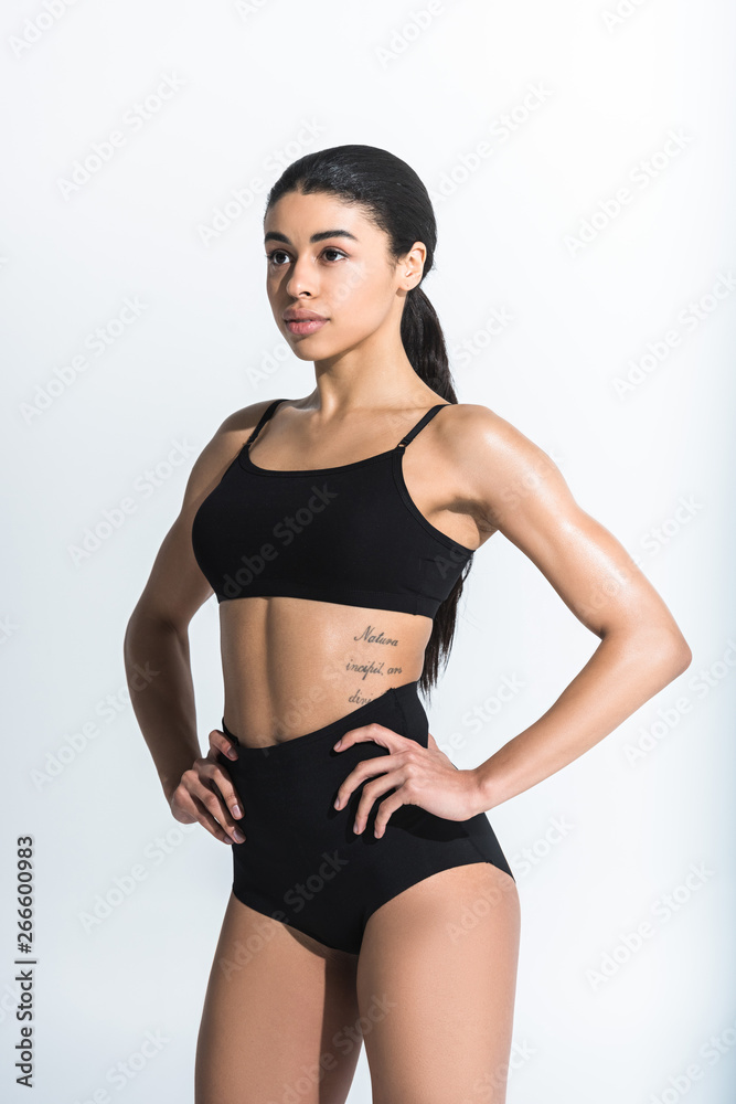 beautiful sportive african american girl in black sports bra and shorts  holding hands on hips on white background Stock Photo