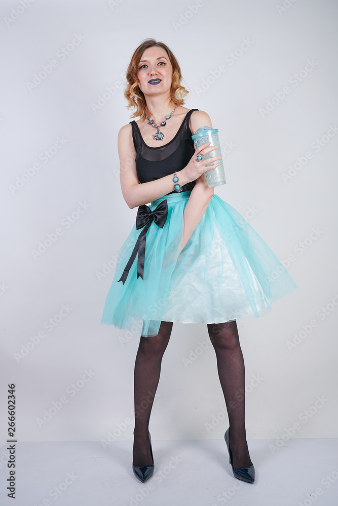 Naklejka premium charming blonde teenager girl in a bright dress with a transparent glass of water on a white background in the Studio