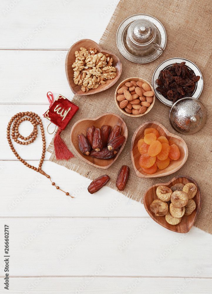 Ramadan iftar party concept. Islamic holy book Quran and rosary beads with delicious dates, dried figs, dried apricots, walnuts, almonds, raisins on bamboo plates on a white wooden table background. Ramadan iftar party concept. Islamic holy book Quran and rosary beads with delicious dates, dried figs, dried apricots, walnuts, almonds, raisins on bamboo plates on a white wooden table background.