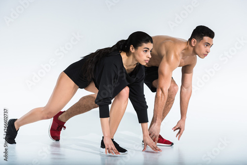 sportive african american girl and athletic mixed race man standing in start position on white