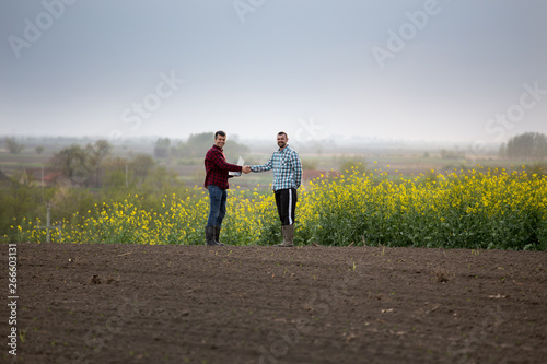 Farmers shaking hands in rapeseed field