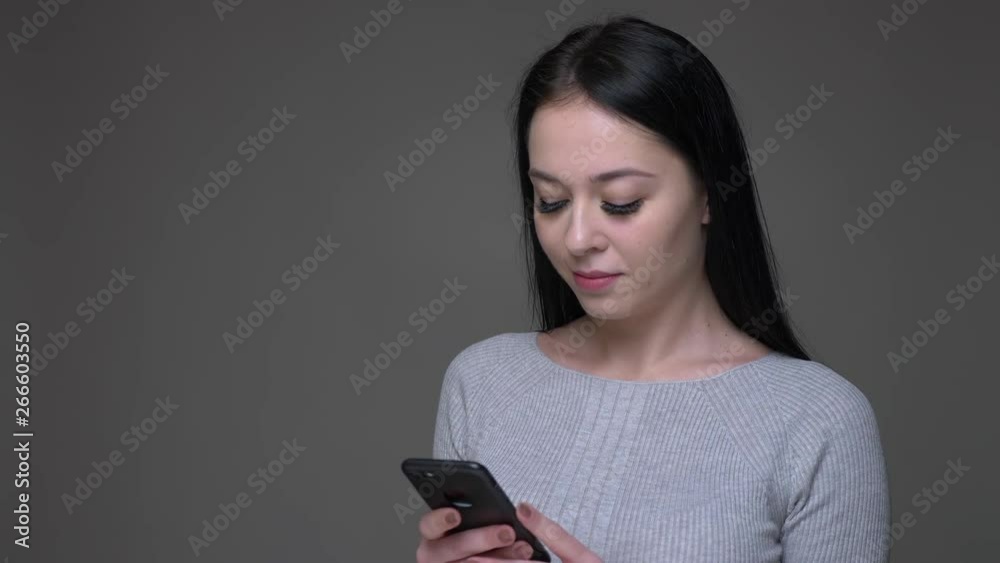 Closeup shoot of young pretty brunette caucasian female using the phone with background isolated on gray Closeup shoot of young pretty brunette caucasian female using the phone with background isolated on gray