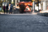 Blurred background, repair roads. Road construction. New, just laid asphalt, leaves from a tree on the road.