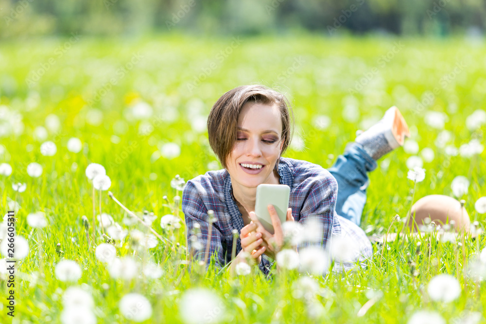 Beautiful woman lying on a sunny meadow with dandelin and talking on the phone Beautiful woman lying on a sunny meadow with dandelin and talking on the phone