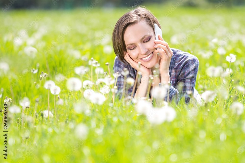 Beautiful woman lying on a sunny meadow with dandelin and talking on the phone Beautiful woman lying on a sunny meadow with dandelin and talking on the phone