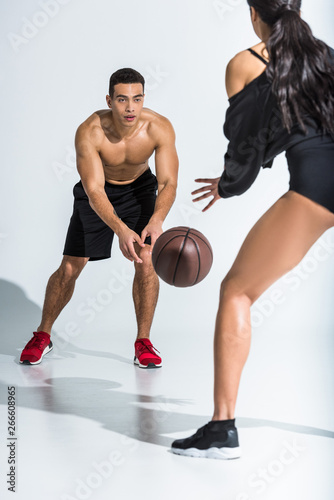 sportive multicultural man and woman playing ball on white background