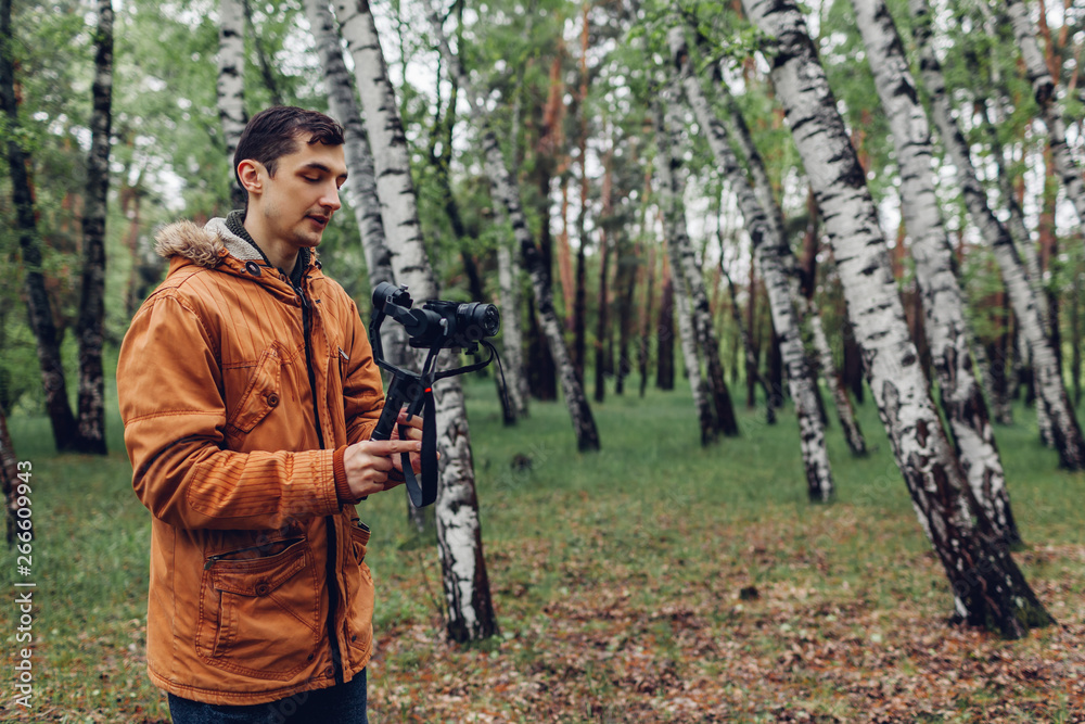 Naklejka premium Videographer filming spring forest. Man using steadicam and camera to make footage. Video shoot