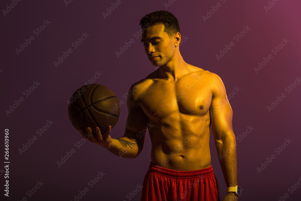 handsome athletic mixed race man holding brown ball on purple background handsome athletic mixed race man holding brown ball on purple background