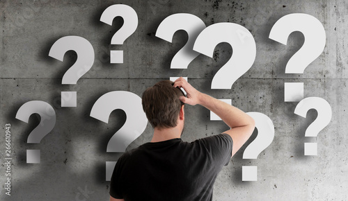 rear view of puzzled man scratching his head against concrete wall filled with question marks photo