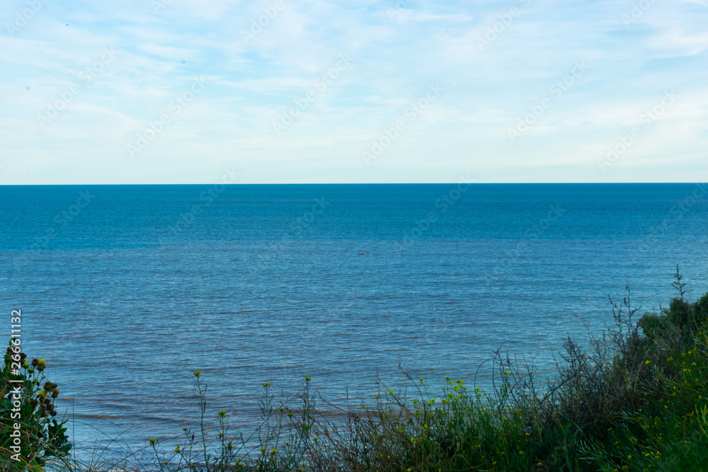 Sea view between two cliffs with vegetation, horizon line and blue sky with clouds.